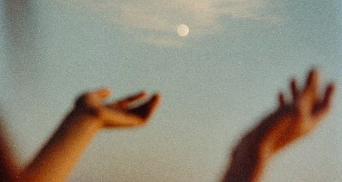 Hands reaching up to a pale moon in a dusk sky